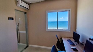 Een kamer met een glazen deur die leidt naar een balkon, een bureau met een computer en uitzicht op zee.