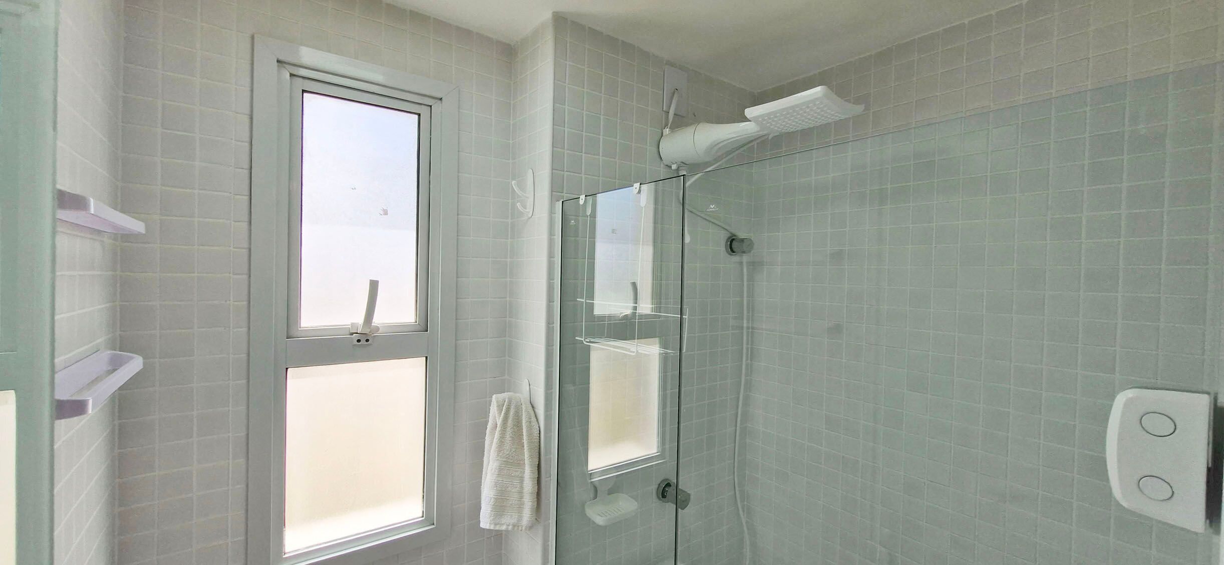 Un baño con cabina de ducha de vidrio, una ventana y una toalla colgada en la pared.