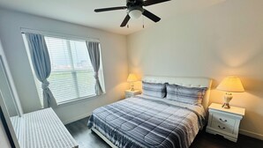 Een slaapkamer met een bed, twee nachtkastjes met lampen, een plafondventilator, een raam met gordijnen en een nachtkastje.