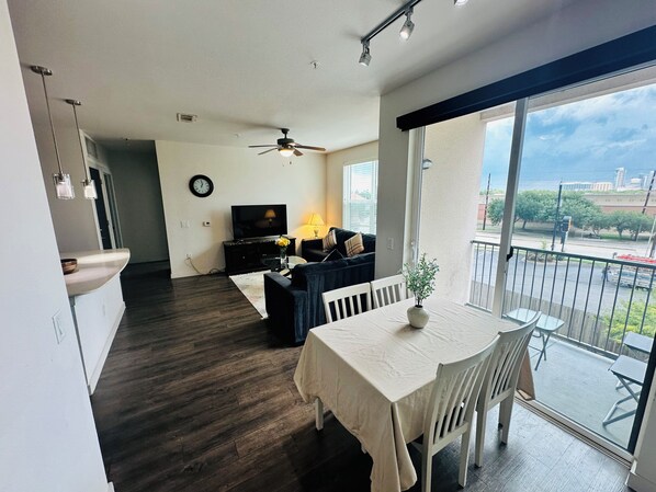 Een moderne woonkamer met een eethoek, een televisie en een balkon met uitzicht op de stad.
