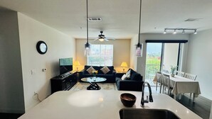 Een moderne keuken met een centraal eiland, een eethoek met tafel en stoelen, een bank en een plafondventilator.
