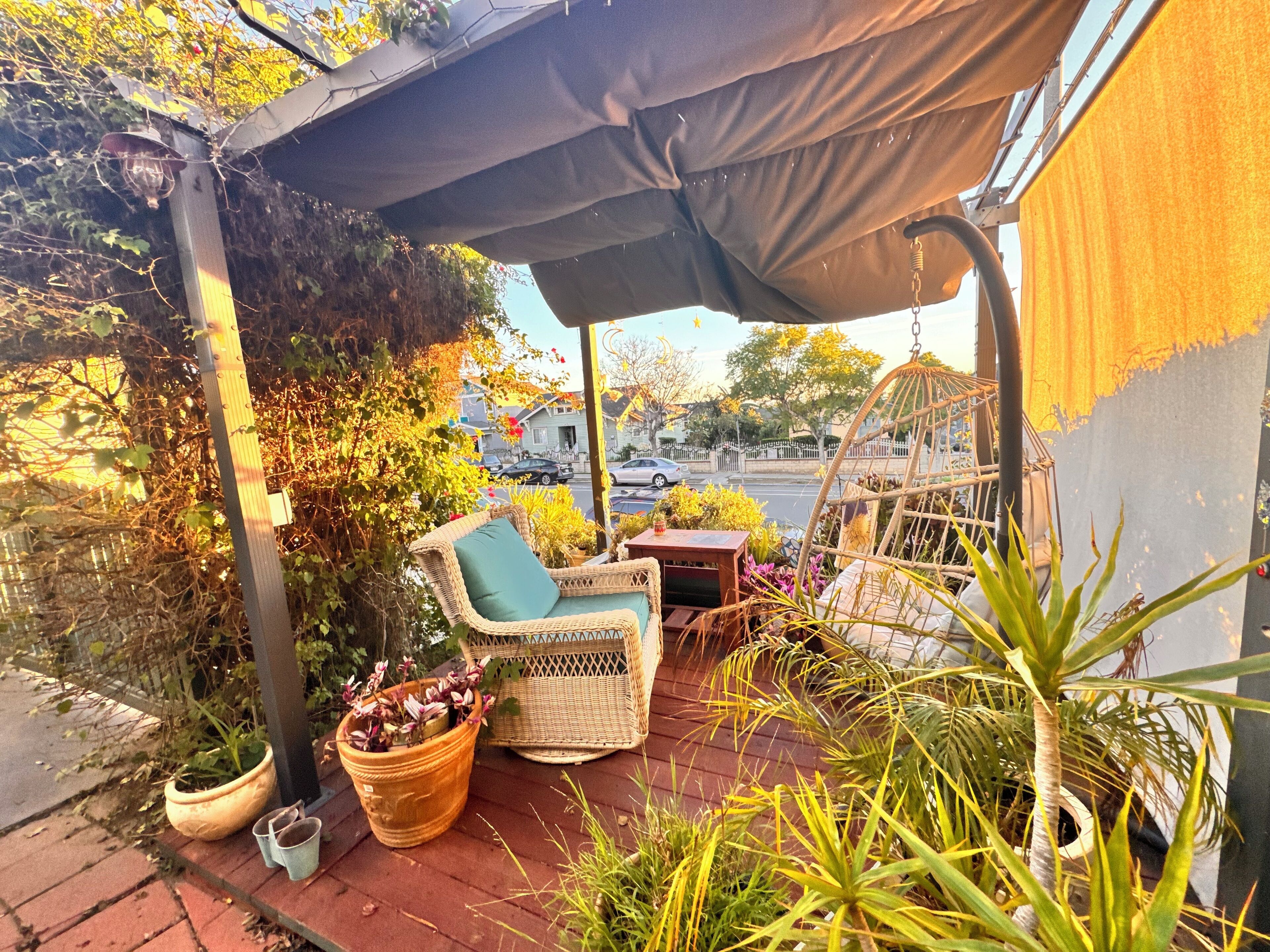 A covered patio with wicker furniture, potted plants, and a hanging chair.