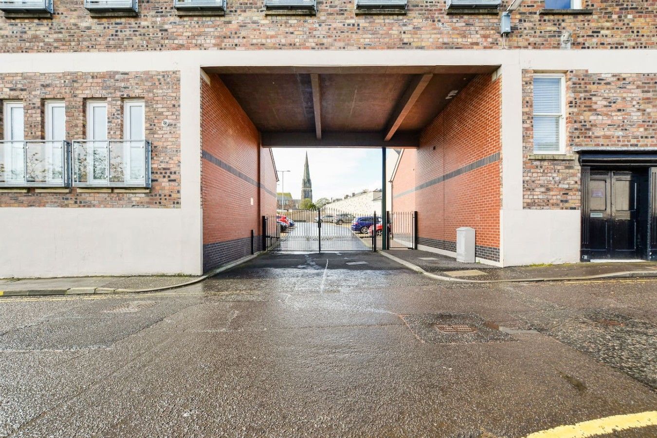 A building entrance with a brick facade, a metal gate, and a paved driveway.