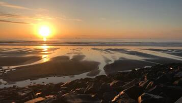 Eine Strandansicht mit Felsen und ruhigem Wasser, das den Sonnenuntergang spiegelt.