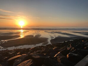 A beach scene with rocks and calm water reflecting the sunset.
