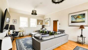 A spacious living room with a large grey sectional sofa, a flat-screen TV, and a ceiling fan.