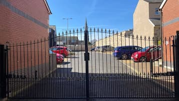 A gated parking area with multiple cars parked, a clear sky, and a building with a brick facade in the background.
