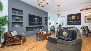 A modern living room with a grey sofa, wooden coffee table, and a chandelier. There are wall-mounted shelves with decorative items and a large framed sign.
