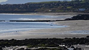 Un paysage côtier avec une plage, une côte rocheuse et des collines à l’horizon.