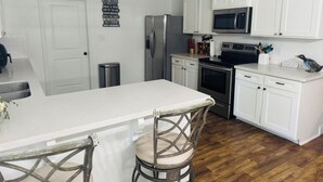 Een moderne keuken met witte kasten, roestvrijstalen apparatuur en een centraal eiland met barstoelen.