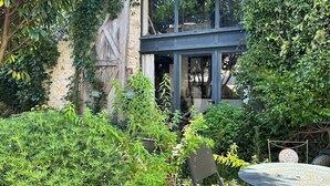 Un espace extérieur aménagé dans un style rustique, avec une table et des chaises, entouré d’une végétation luxuriante et d’un mur en pierre.
