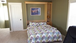 Une chambre à coucher avec un lit, une porte, une étagère avec une lampe et un tableau au mur.