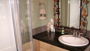 Une salle de bain dotée d’une porte de douche en verre, d’un lavabo blanc et d’un miroir orné d’un motif décoratif en forme de feuilles.