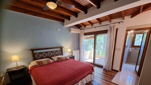 A bedroom with a wooden ceiling, a bed with a red blanket, two bedside lamps, and a view of the outside through a glass door. - Bosque De Bohemia Delta Tigre (Partido de Tigre)