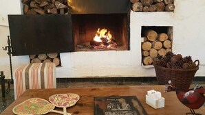 A cozy room with a fireplace, a table with decorative plates, a book, and a basket of pinecones. - Bosque De Bohemia Delta Tigre (Partido de Tigre)