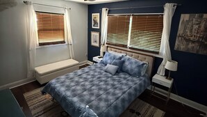 Una camera da letto con un letto, un comodino, una lampada, una ventola a soffitto e una finestra con persiane.
