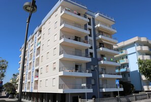 A multi-story residential building with balconies, a pedestrian crossing sign, and a street lamp. - Modern Flat With sea View (San Michele al Tagliamento)
