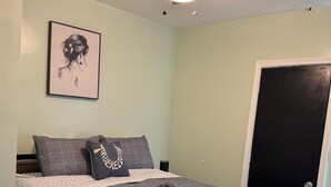 Ein Schlafzimmer mit Bett, Deckenventilator, gerahmtem Bild an der Wand und einer Tür.