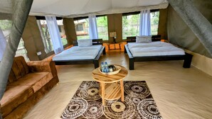 A tent-style accommodation with two beds, a sofa, a table with water bottles, and a patterned rug. - Double G Safaris And Camp Mikumi (Dar es Salaam)
