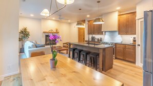 A modern kitchen with wooden cabinets, a central island with bar stools, pendant lighting, and a dining area with a wooden table and chairs. - Luxury Mountain-Modern Retreat 3BR near Glacier National Park & Whitefish (Columbia Falls)