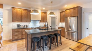 A modern kitchen with wooden cabinets, stainless steel appliances, and a central island with stools. - Luxury Mountain-Modern Retreat 3BR near Glacier National Park & Whitefish (Columbia Falls)
