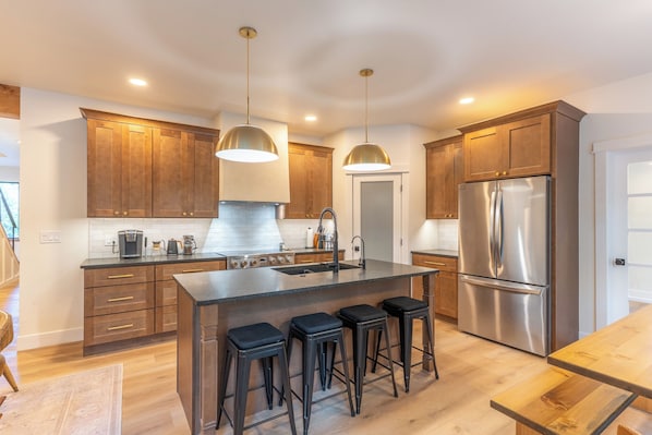 Cocina moderna con armarios de madera, electrodomésticos de acero inoxidable y una isla central con taburetes.