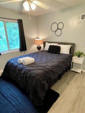 A bedroom with a large bed, a bedside table, a lamp, and a view of greenery outside. - Classy 2 Bedroom Home (Belton)