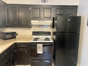 A kitchen with dark cabinets, a black refrigerator, a white stove, and a microwave. - Classy 2 Bedroom Home (Belton)