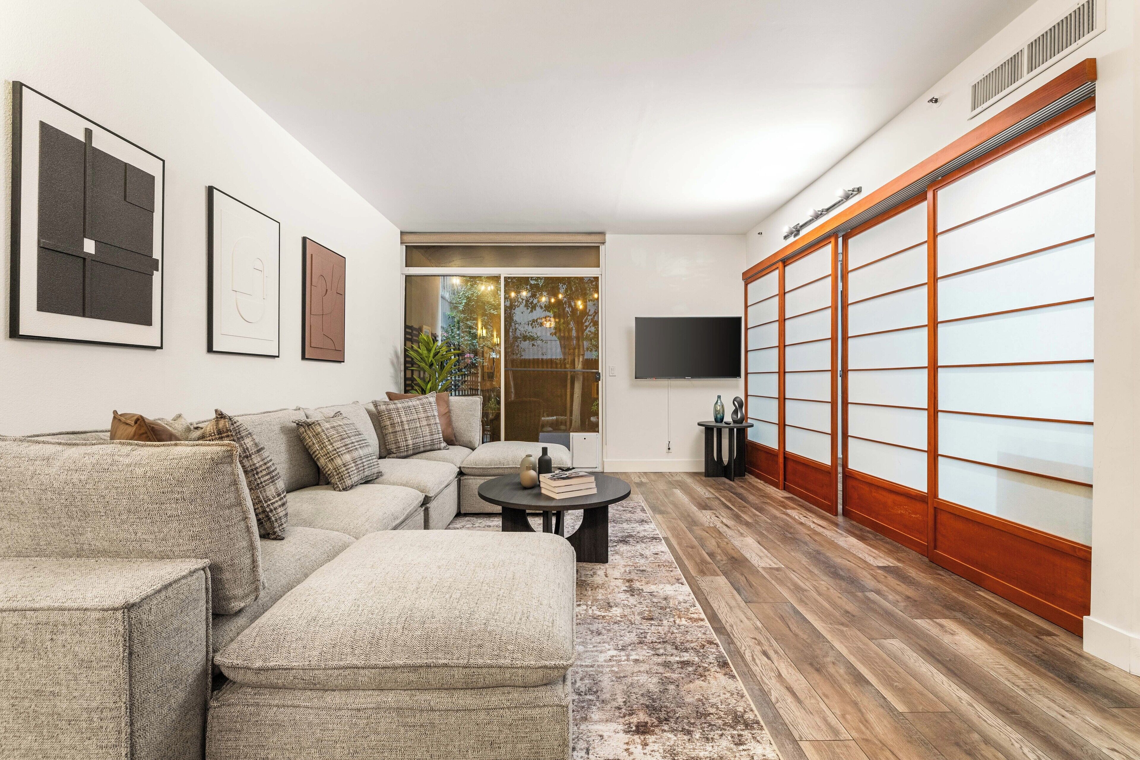 Un salon moderne avec un canapé d’angle, une table basse et une porte-fenêtre coulissante donnant sur un balcon.