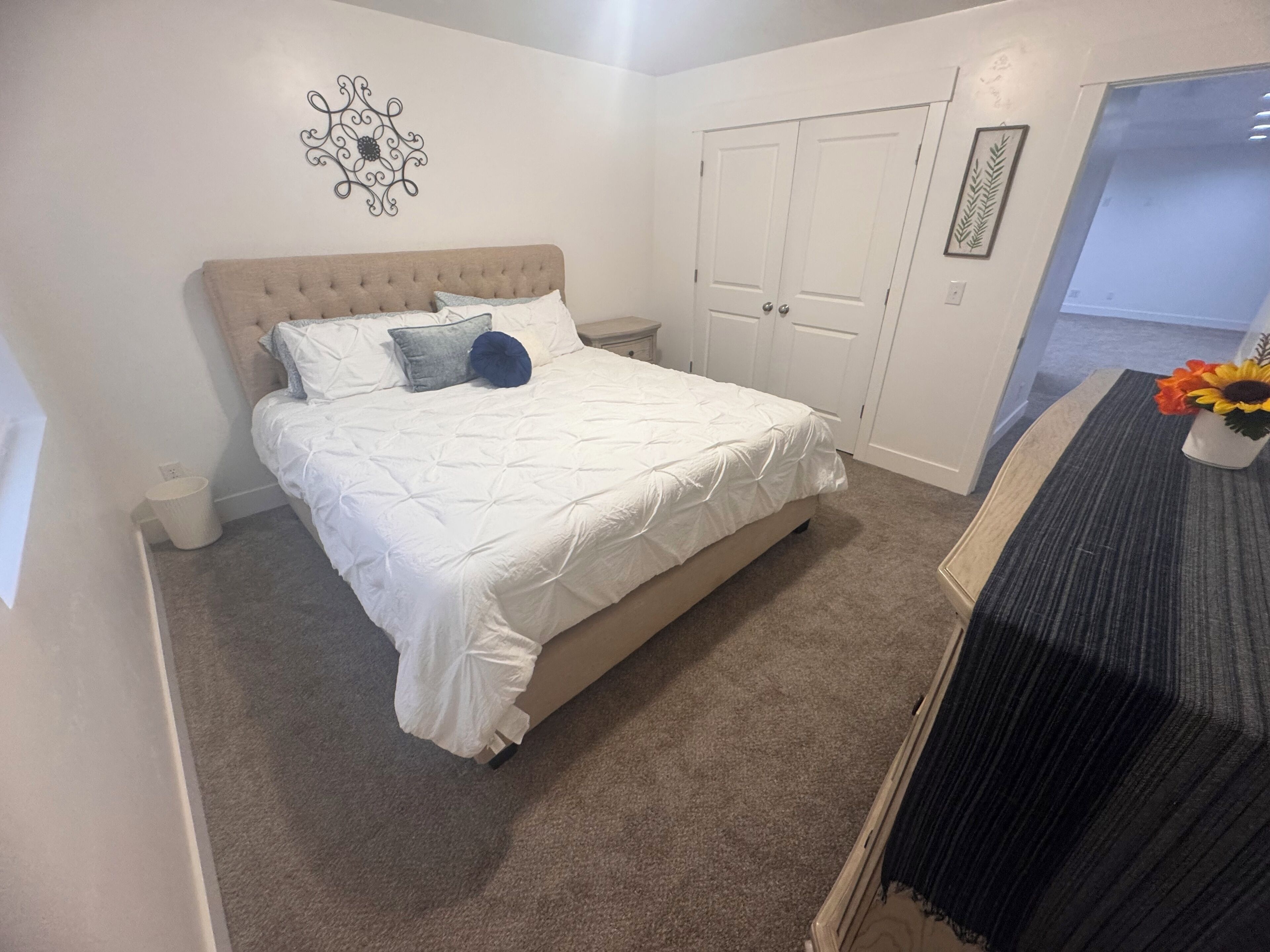 Een slaapkamer met een groot bed, een nachtkastje, een dressoir en een deur naar een andere kamer.