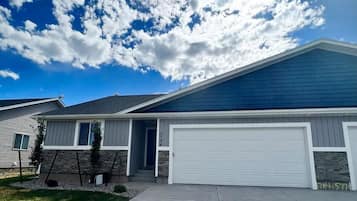 A single-story house with a garage, a stone foundation, and a clear blue sky with clouds.