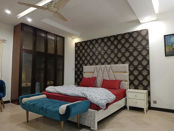 A bedroom with a bed, a nightstand, a bench, a wardrobe, and a ceiling fan.