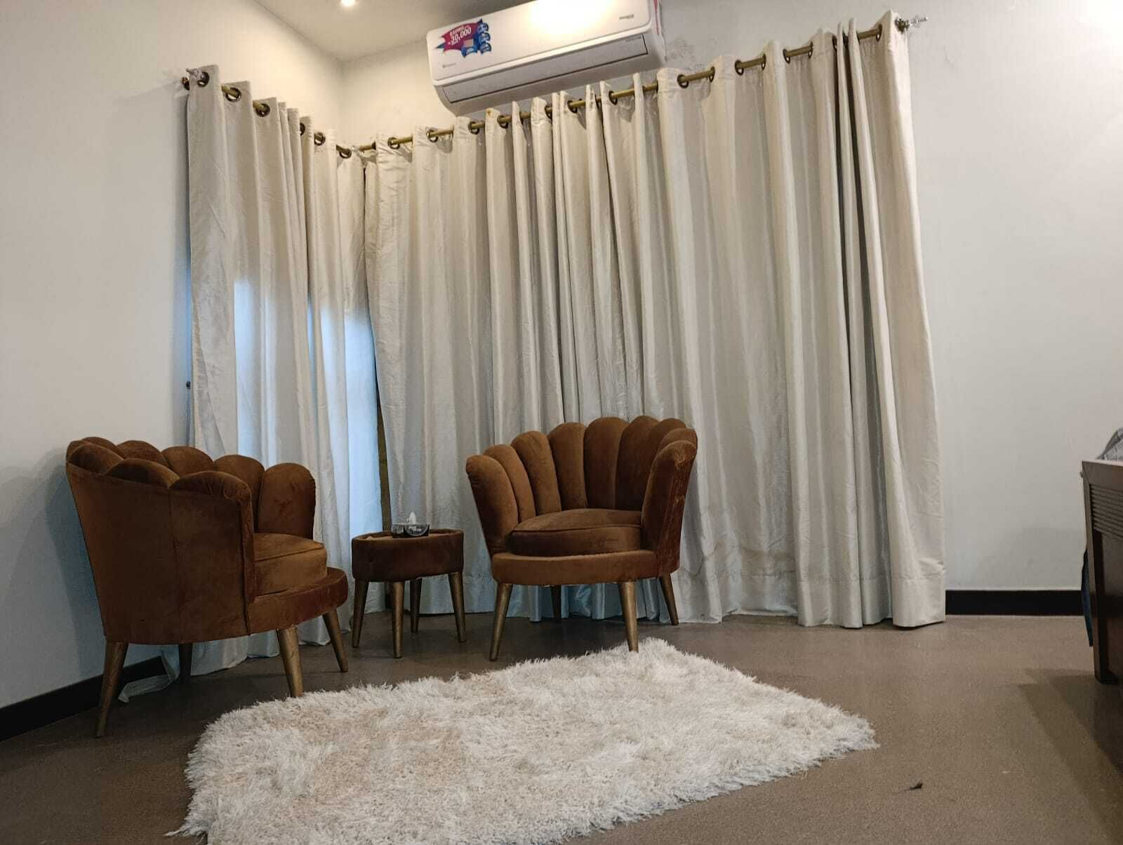 Un salon avec deux fauteuils marron, un tapis à poils longs blanc et un fond de rideau blanc.