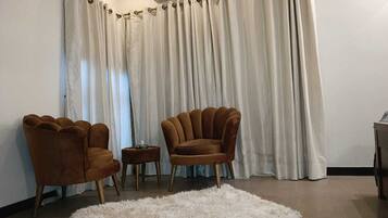 Un salon avec deux fauteuils marron, un tapis à poils longs blanc et un fond de rideau blanc.