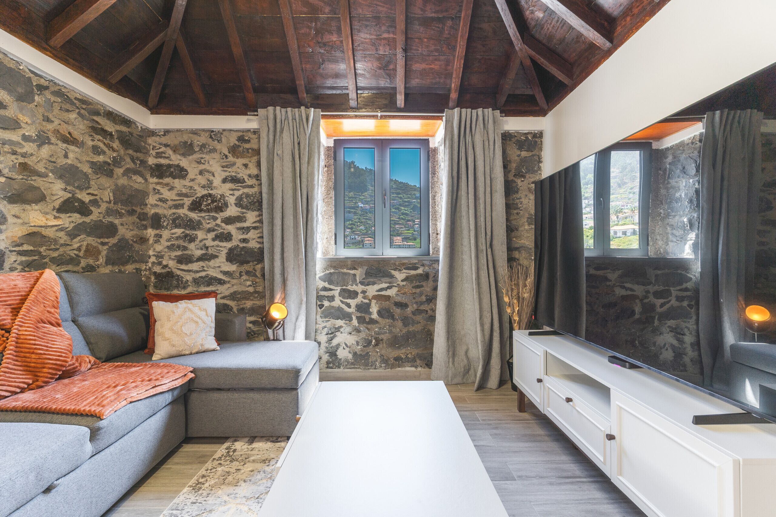 Una sala de estar con una pared de piedra, un sofá, una mesa de centro y un televisor.