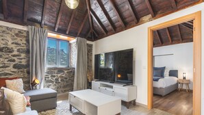 A cozy room with a stone wall, a fireplace, a large TV, and a bed with a view of the outdoors.