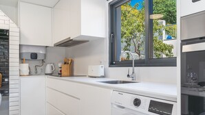 A modern kitchen with white cabinetry, a built-in dishwasher, and a window with a view of trees.