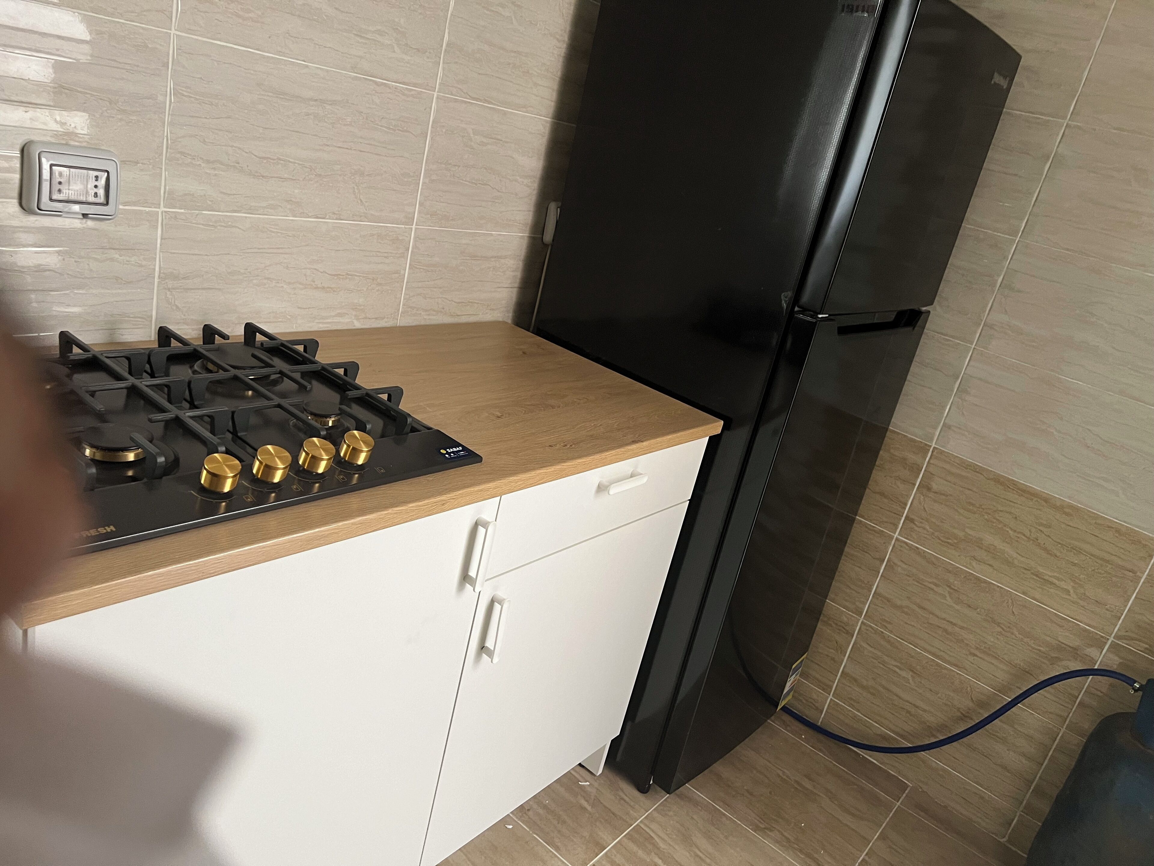 Une cuisine équipée d’une cuisinière à gaz, d’un réfrigérateur noir et d’un dosseret carrelé.