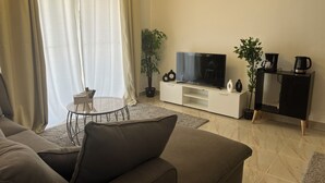 A living room with a sofa, a TV, a coffee maker, and a plant.