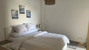 A neatly made bed with white bedding, a bedside table with a lamp, and three framed pictures on the wall.