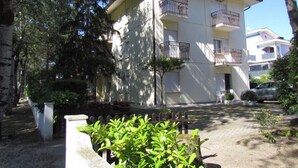 A multi-story building with balconies, surrounded by greenery and a gravel driveway. - Luminous Flat Near the Beach (San Michele al Tagliamento)