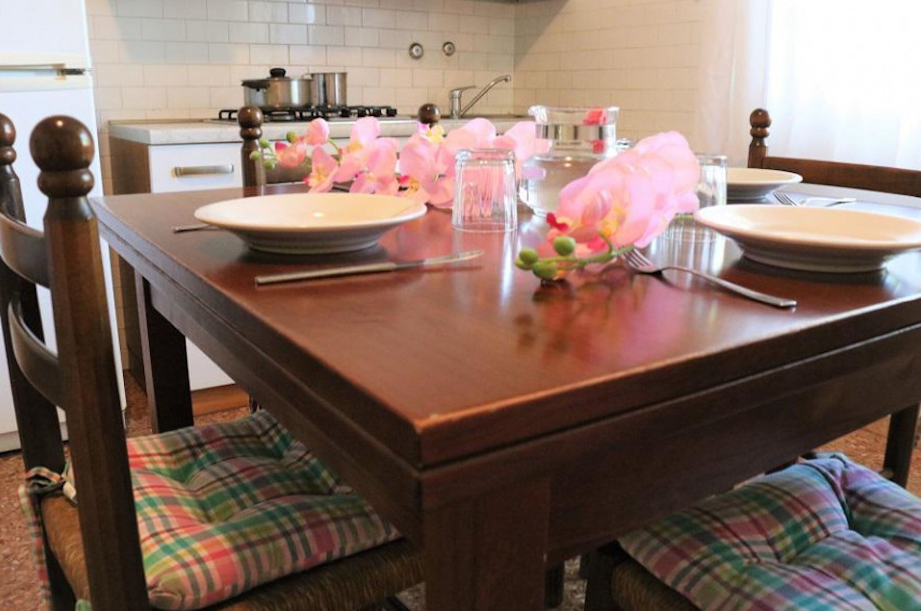 Une table à manger dressée avec des assiettes, des couverts et des fleurs roses.
