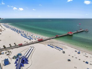 Ein Strand mit einem Steg, der ins Meer führt, Reihen von Sonnenschirmen und einer Wasserrutsche.