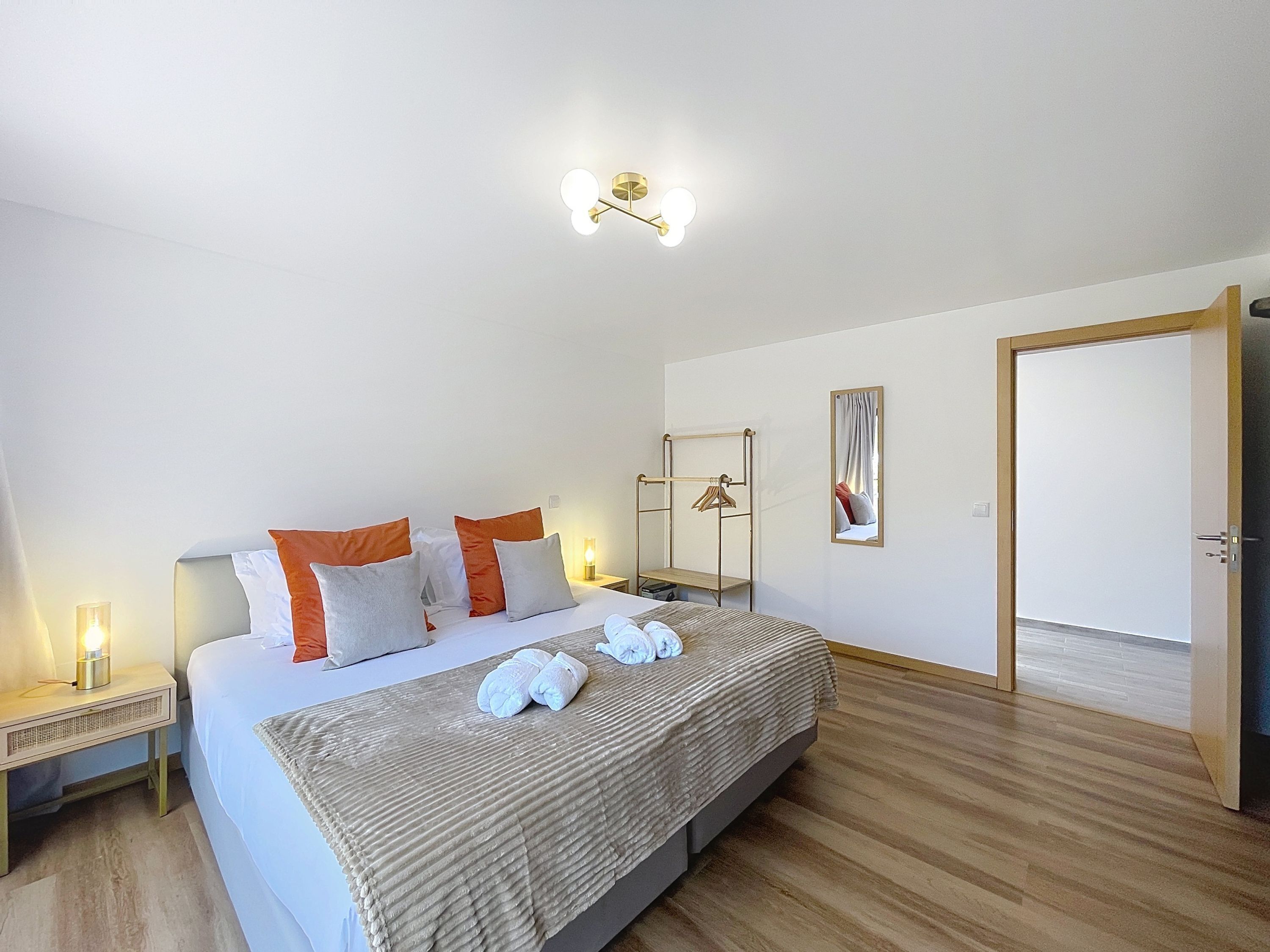 Une chambre à coucher bien rangée, avec un lit, des tables de chevet, un luminaire suspendu, un miroir et une porte.