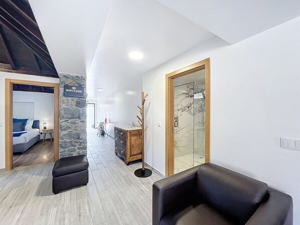 A modern interior with a stone accent wall, a wooden cabinet, a glass shower enclosure, and a seating area with a bench. - Juliana s House 1 by Atlantic Holiday (Ribeira Brava)