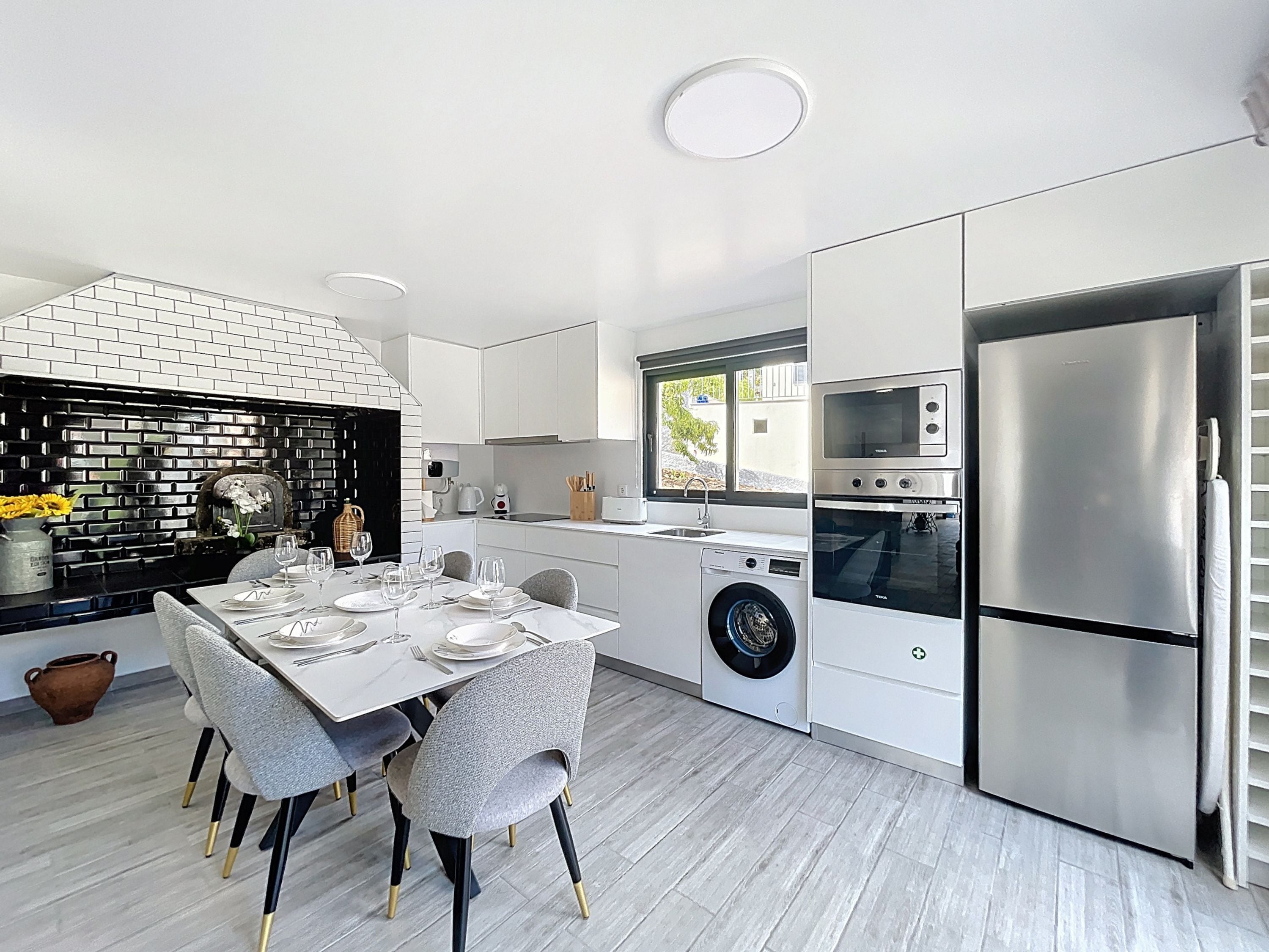 Una cocina moderna con armarios blancos, horno empotrado, refrigerador de acero inoxidable y comedor con mesa dispuesta para cuatro.