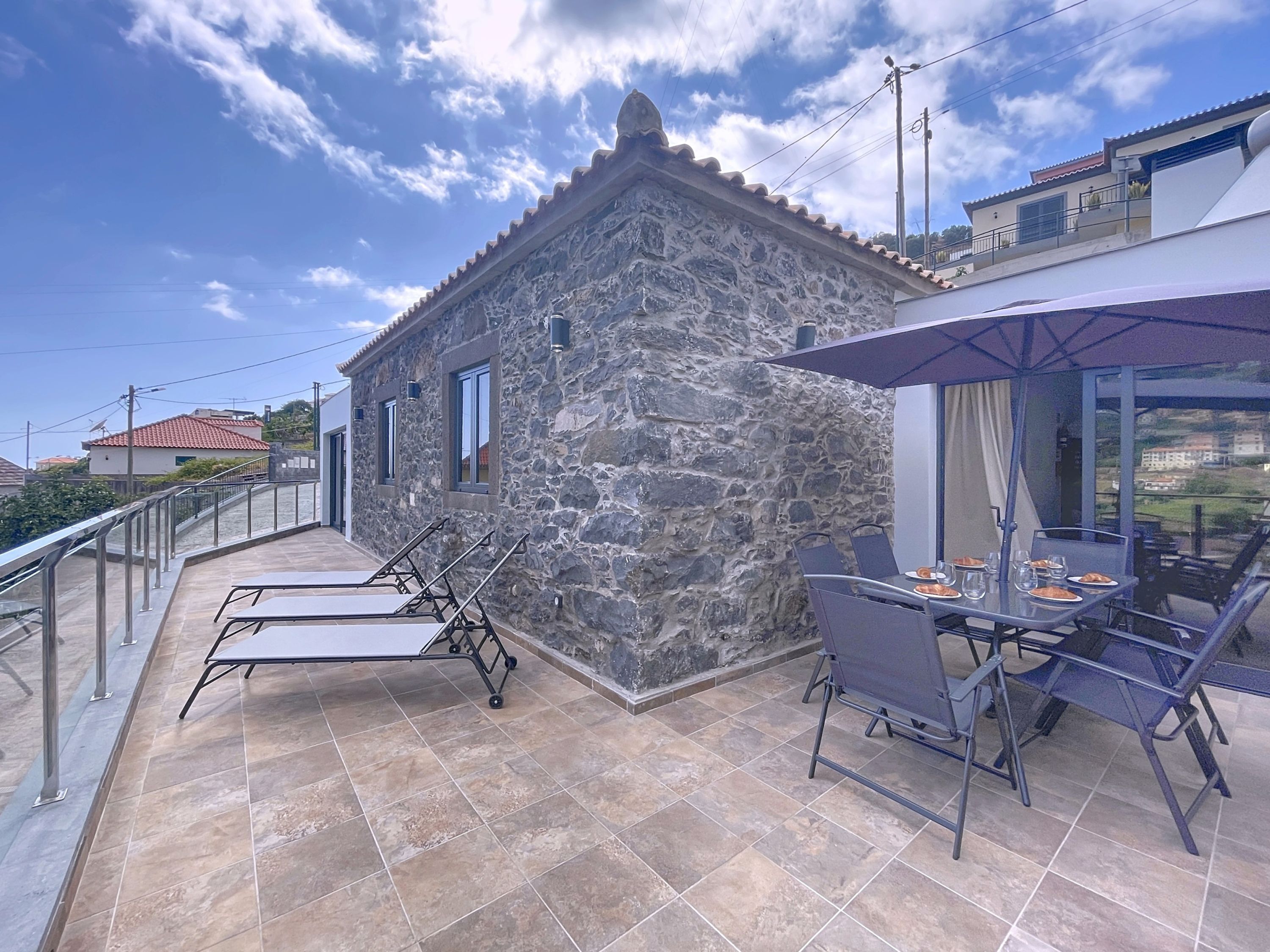 A stone building with a balcony, a table with chairs, and a view of the surrounding area.