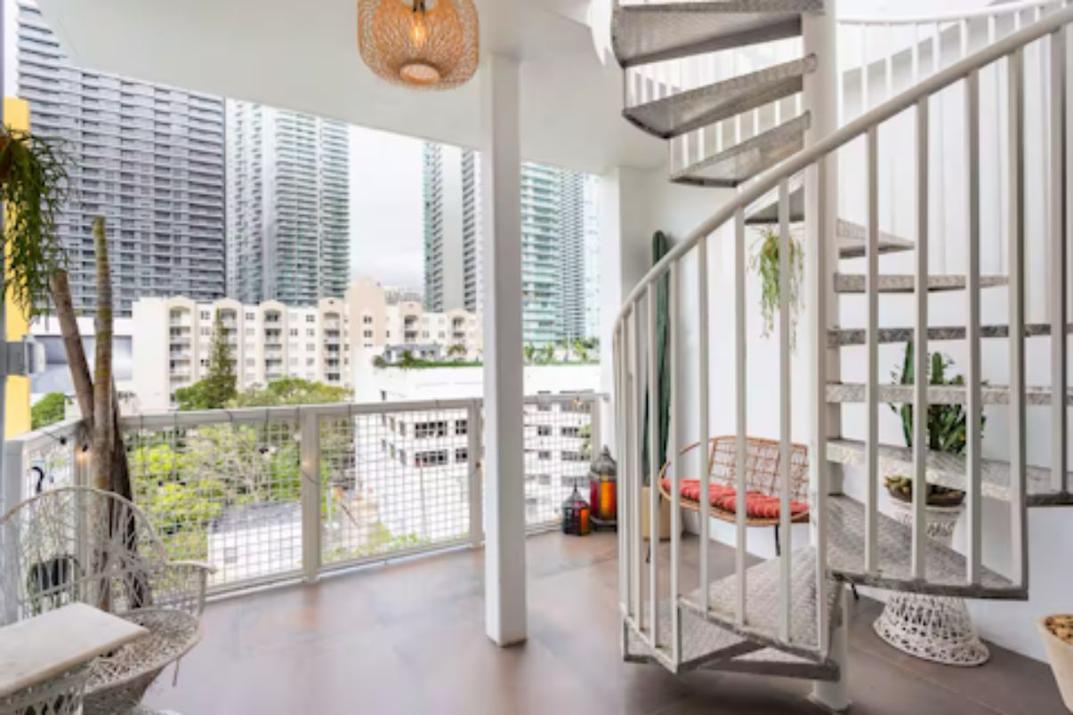 Un balcon spacieux offrant une vue sur les immeubles de grande hauteur, avec une balustrade blanche et un luminaire suspendu.