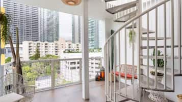 Un balcon spacieux offrant une vue sur les immeubles de grande hauteur, avec une balustrade blanche et un luminaire suspendu.