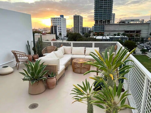 Eine Dachterrasse mit weißer Couch, Korbstühlen und Topfpflanzen.